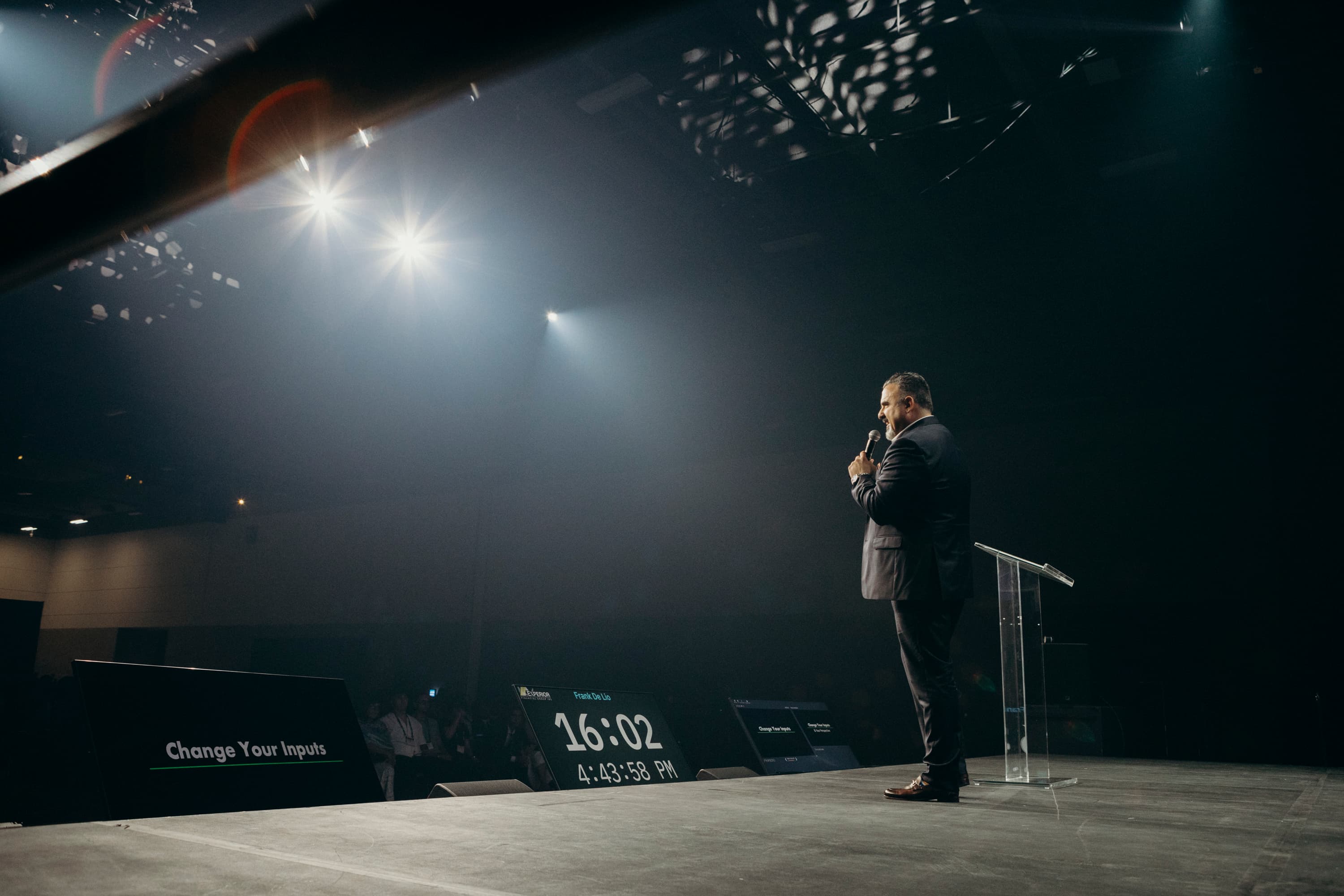 Frank Delio speaking on stage under spotlights